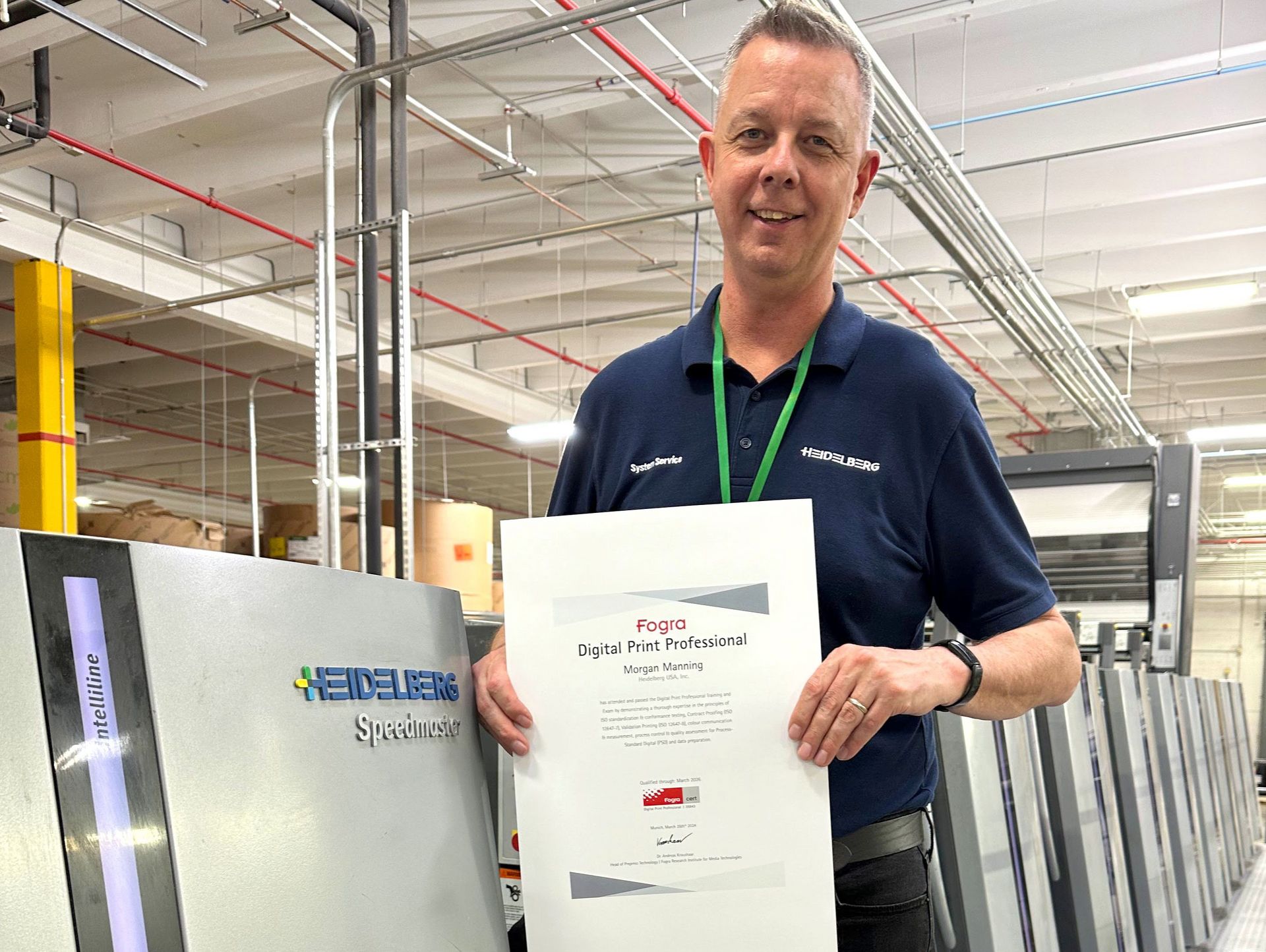 Man with blue shirt holds a paper in both hands in front of a printing machine